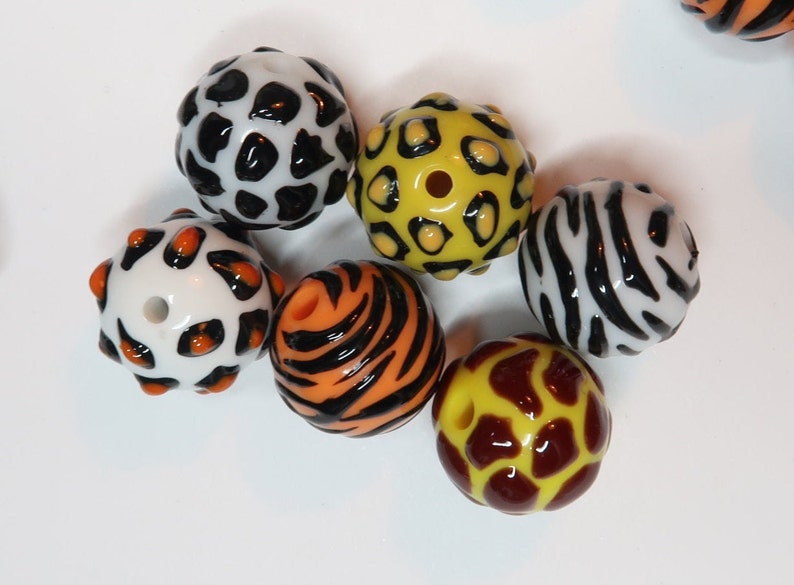 May include: Six colourful glass beads with different animal print patterns. The beads are white, black, orange, yellow, brown, and red.