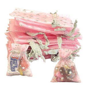 May include: A stack of pink organza bags with silver star print and silver ribbon ties. The bags are filled with small candies and trinkets. The text "well played" is visible on one of the bags.