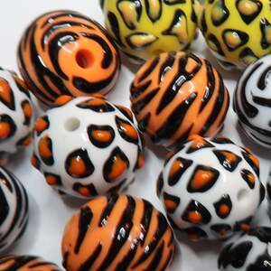 May include: A collection of colourful round beads with various animal print designs. The beads feature black, orange, white, and yellow colours with patterns of stripes, spots, and swirls.