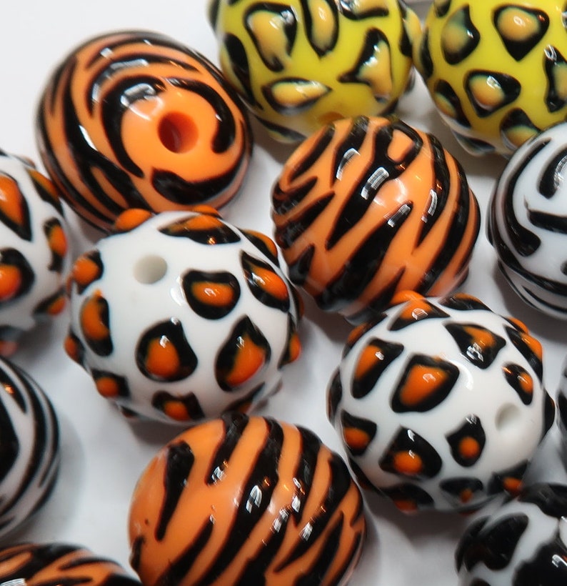 May include: A collection of colourful round beads with various animal print designs. The beads feature black, orange, white, and yellow colours with patterns of stripes, spots, and swirls.
