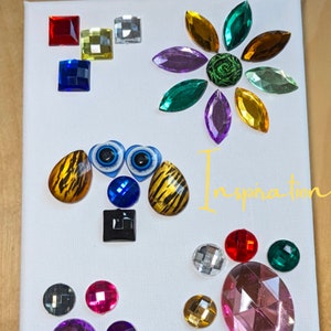 Puede incluir: Un lienzo blanco con brillantes y piedras preciosas de vidrio de colores dispuestos en un dise&ntilde;o caprichoso. El dise&ntilde;o incluye una flor, una cara de animal de dibujos animados y un grupo de piedras preciosas. La palabra "Inspiration" est&aacute; escrita en amarillo en el lienzo.