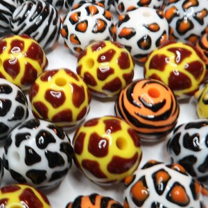 May include: Assortment of colourful round beads with various animal print designs, including zebra, leopard, giraffe, and tiger patterns. The beads are made of plastic and have a glossy finish.