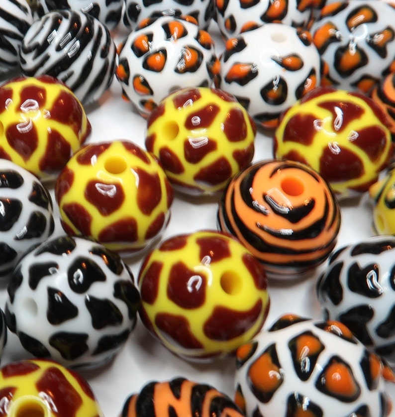 May include: Assortment of colourful round beads with various animal print designs, including zebra, leopard, giraffe, and tiger patterns. The beads are made of plastic and have a glossy finish.