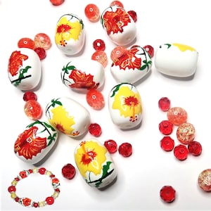 May include: A collection of white ceramic beads with hand-painted yellow and red hibiscus flowers. The beads are scattered on a white surface with red and orange glass beads.
