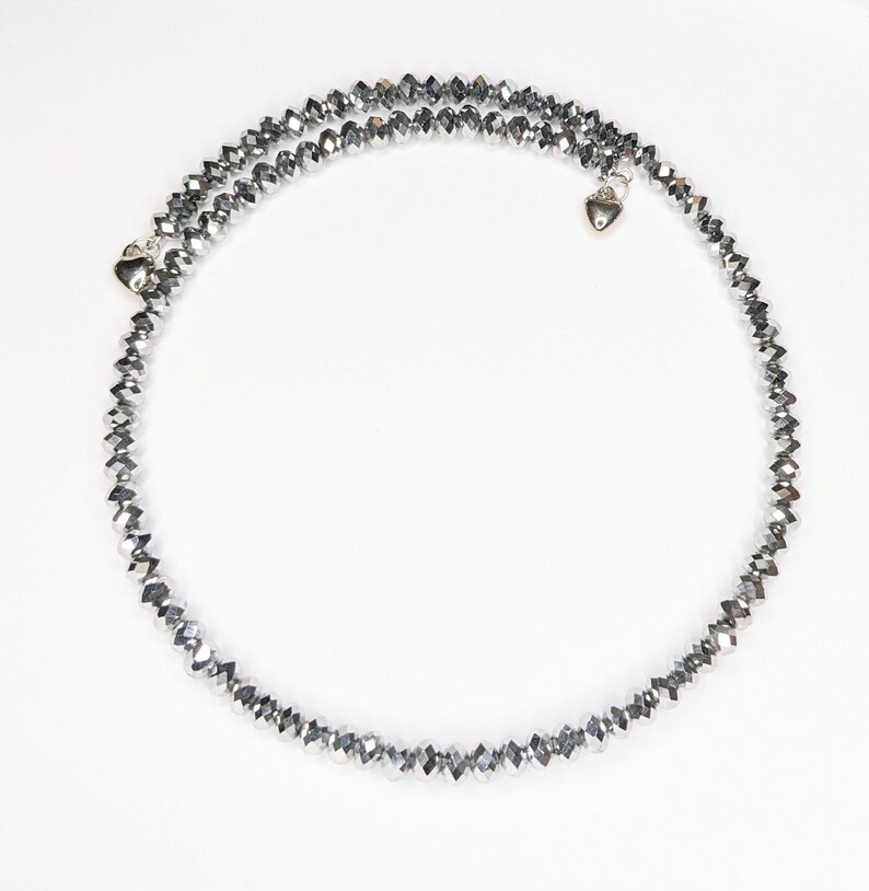 K&ouml;nnte beinhalten: Eine silberne Kristallkette mit zwei herzf&ouml;rmigen Anh&auml;ngern. Die Kette besteht aus kleinen, facettierten Kristallen, die auf einer silbernen Kette aufgereiht sind.