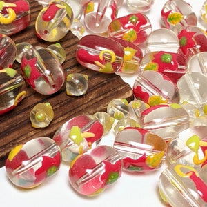 May include: A collection of clear glass beads with red, yellow, and green floral designs. The beads are oval shaped and have a glossy finish.