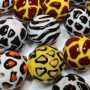 May include: A collection of colourful glass beads with various animal print designs, including zebra, leopard, and giraffe patterns.