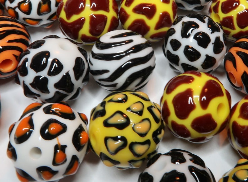 May include: A collection of colourful glass beads with various animal print designs, including zebra, leopard, and giraffe patterns.