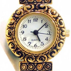 May include: Gold-tone watch with a round face and ornate details. The watch face has black Roman numeral hour markers and a white background with the word "QUARTZ" printed on it.