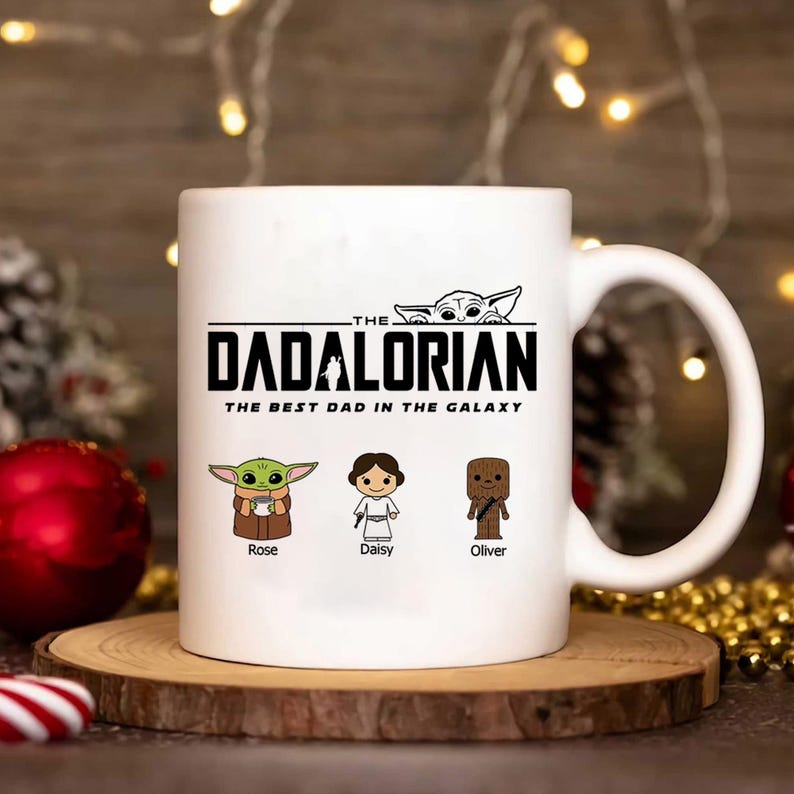 May include: A white ceramic mug featuring the text The Dadalorian The Best Dad In The Galaxy in black lettering. Below the text are three cartoon characters labeled Rose, Daisy, and Oliver, with a small character peeking over the top text.