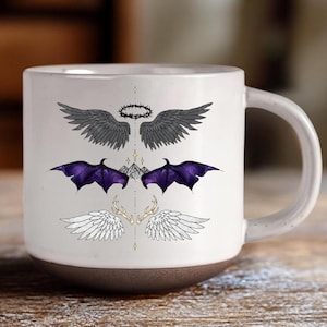 Könnte beinhalten: Weißer Keramikbecher mit dunkelbraunem Boden, mit drei Sätzen illustrierter Flügel: graue Engelsflügel, lila Fledermausflügel und weiße Engelsflügel mit Geweih. Dargestellt sind auch eine Dornenkrone und Bergspitzen.