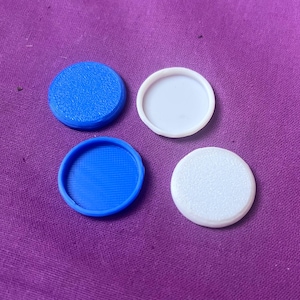 Könnte beinhalten: Vier kreisförmige Scheiben, die in einem Quadrat angeordnet sind. Zwei Scheiben sind leuchtend blau und zwei sind weiß. Eine blaue Scheibe hat eine strukturierte Oberfläche, während die andere eine glatte, vertiefte Mitte aufweist. Eine weiße Scheibe ist glatt, die andere strukturiert.