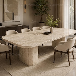 Puede incluir: Una gran mesa de comedor rectangular con una superficie de piedra travertino beige pulida y una base de pedestal de piedra maciza a juego, rodeada por ocho sillas tapizadas con patas de madera oscura y respaldos curvos en tela crema neutra.