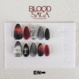 Può includere: Un set di dieci unghie finte a mandorla con vari disegni tra cui un paesaggio al tramonto, il testo Blood Saga, Just come kiss me and bite me, un emblema a croce argentata, una luna rossa e il testo EN- su un cartoncino bianco.