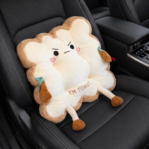 以下が含まれることがあります： 「I'M TOAST」の文字と漫画の顔が描かれた、トースト型の車のシートクッション。 クッションは白い中心部、茶色の地殻、小さな茶色の足を持っています。 黒い車のシートに置かれています。