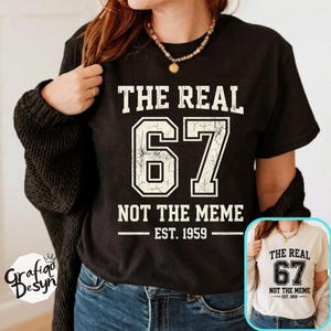 May include: Black t-shirt with white text that reads "THE REAL 67 NOT THE MEME EST. 1959". The number 67 is large and centered. A smaller image of the same shirt is in the lower right corner.