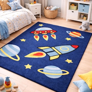 以下が含まれることがあります： 子供部屋用の宇宙をテーマにした紺色のラグ。ロケット、惑星、星、UFOが赤、黄、青で描かれています。