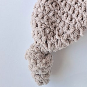 Pu&ograve; includere: Primo piano di una coperta all'uncinetto beige con una superficie testurizzata e soffice.