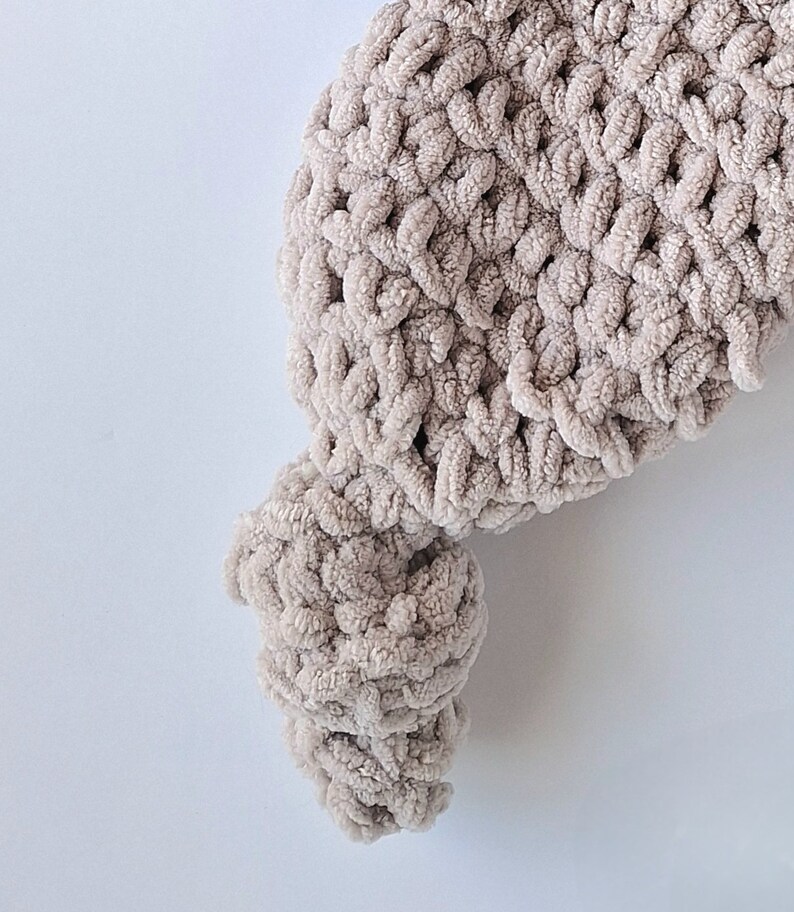 Pu&ograve; includere: Primo piano di una coperta all'uncinetto beige con una superficie testurizzata e soffice.