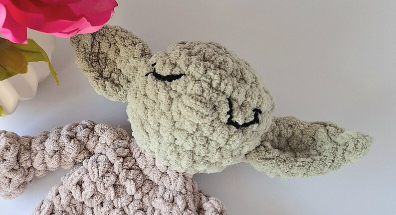 Pu&ograve; includere: Un giocattolo di peluche verde all'uncinetto con un viso sorridente e grandi orecchie. Il giocattolo &egrave; fatto di filato morbido e testurizzato e ha un corpo marrone chiaro.
