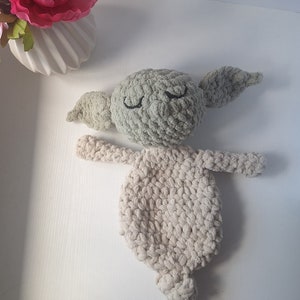 Pu&ograve; includere: Un giocattolo di peluche lavorato a uncinetto a forma di personaggio con grandi orecchie, occhi chiusi e corpo beige. Il giocattolo &egrave; realizzato con un filato morbido e peloso e ha una testa verde.