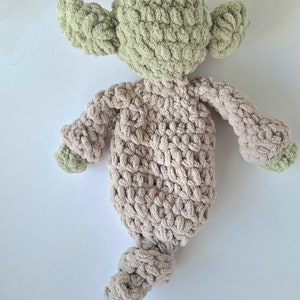 Pu&ograve; includere: Un giocattolo di peluche lavorato a uncinetto a forma di personaggio con orecchie verdi e corpo marrone. Il giocattolo &egrave; sdraiato sulla schiena con le braccia distese.