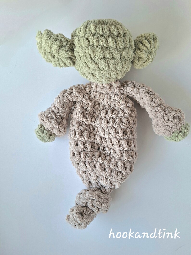 Pu&ograve; includere: Un giocattolo di peluche lavorato a uncinetto a forma di personaggio con orecchie verdi e corpo marrone. Il giocattolo &egrave; sdraiato sulla schiena con le braccia distese.