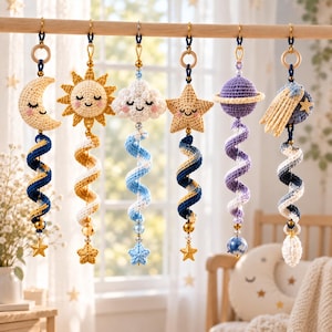 May include: Six hanging celestial ornaments featuring crocheted figures of a crescent moon, sun, cloud, star, planet with rings, and a comet. Each figure has a smiling face and is attached to a spiraling yarn tail with beads and a small star.