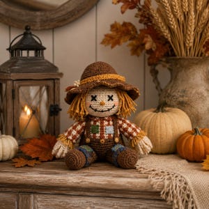 May include: A crochet scarecrow doll wearing a brown hat with a yellow band, a red and white checkered shirt, and brown overalls with small green and blue patches. The doll has yellow yarn hair, black stitched eyes, and a stitched smile.