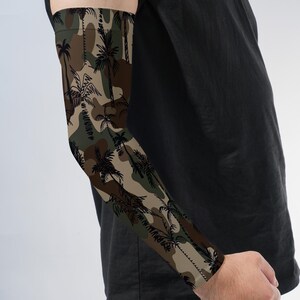 May include: An arm sleeve featuring a camouflage pattern in shades of brown, tan, and dark green, overlaid with a repeating black silhouette print of palm trees. The sleeve extends from the upper arm to the wrist, covering the forearm.