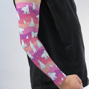 May include: An arm sleeve featuring a repeating pattern of white polar bears on a background of wavy pink, magenta, and orange stripes. The design includes small white dots scattered across the fabric, creating a snowy effect throughout the sleeve.