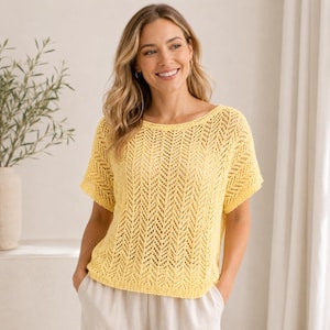 May include: A light yellow, short-sleeved knit top with a scoop neck. The top features a chevron pattern and a loose, airy weave. The model is wearing the top with light-colored pants.