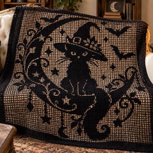 Könnte beinhalten: Eine schwarz-beige gehäkelte Decke mit einem zentralen Motiv einer Katze mit Hexenhut, die auf einer Mondsichel sitzt. Das Muster umfasst Sterne, geschwungene Rankenmotive und fliegende Fledermäuse, alles im gitterartigen Filethäkelstil.