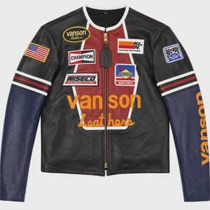 Könnte beinhalten: Eine schwarze Lederjacke mit einem roten Mittelteil, blauen Ärmeln und einem goldenen Reißverschluss. Die Jacke ist mit verschiedenen Aufnähern zum Thema Rennsport verziert, darunter Vanson Leathers, Champion, Wiseco, K&N, Sunoco und Bel-Ray.