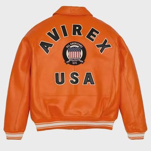 May include: A bright orange jacket featuring the text AVIREX in a black arc across the upper back. Below this, a circular patch displays an American flag with the text ALL AMERICANS ESTABLISHED 1975. The word USA is printed in large black letters.