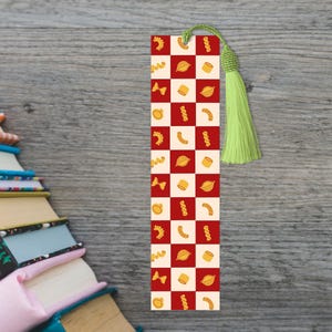 May include: A rectangular bookmark featuring a red and cream checkered pattern decorated with various yellow pasta shapes. The bookmark includes a light green knotted tassel attached to the top center with a small metal eyelet for hanging.