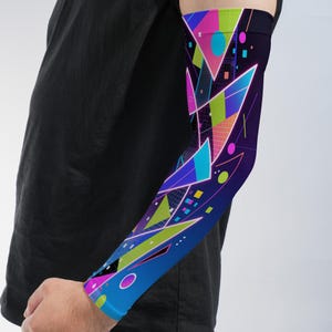 May include: An arm sleeve featuring a dark blue base with a vibrant geometric pattern of triangles, circles, and grid lines in bright shades of pink, lime green, cyan, and yellow. The design covers the entire length of the sleeve from wrist to bicep.