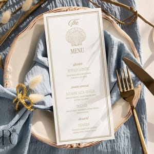 Pode incluir: Um cartão de menu vertical branco com bordas douradas e uma ilustração de concha no topo. O texto diz The MENU, starter BUFFALO CAPRESE, main course SALMONE ALLA GRIGLIA, TAGLIATA e dessert TIRAMISU, com descrições detalhadas abaixo.