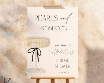 May include: A rectangular sign on a wooden easel featuring the text PEARLS and PROSECCO, WELCOME TO Ophelia's BRIDAL SHOWER, and 17.10.202X. The design includes a watercolor illustration of a champagne coupe glass with a black ribbon and pearls.