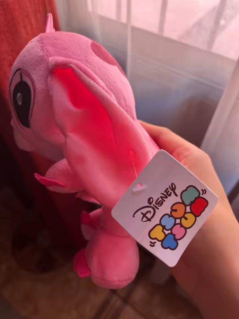 Puede incluir: Un peluche rosa de un personaje con orejas grandes y una etiqueta que dice "Disney Tsum Tsum". El juguete es de color rosa claro con manchas y detalles en rosa m&aacute;s oscuro. La etiqueta es blanca con logotipos coloridos de Disney.