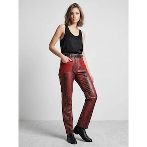 May include: A black sleeveless tank top paired with red and black snakeskin-patterned trousers. The trousers feature a high waist with a black belt, two front pockets with red suede-like accents, and a straight-leg cut reaching the ankles.