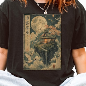 Puede incluir: Camiseta negra con una ilustración de inspiración japonesa. El diseño incluye una isla flotante con un edificio tradicional, una luna llena y grullas. El texto en la imagen está en japonés.