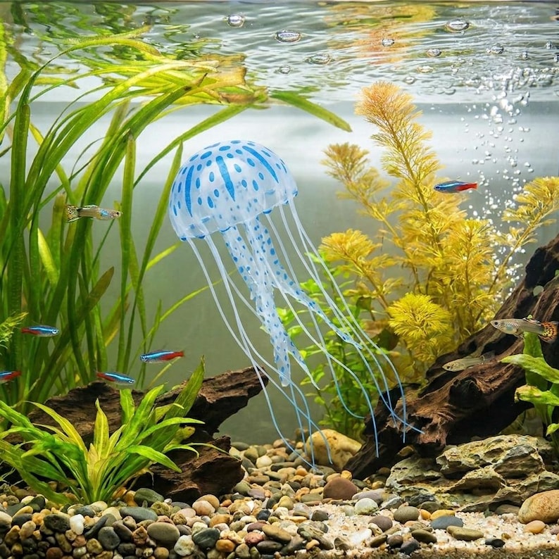 Pu&ograve; includere: Scena di acquario con una decorazione di medusa a pois blu e bianchi con lunghi tentacoli fluttuanti. La vasca include piante vive, piccoli pesci e un substrato di ghiaia, creando un ambiente sottomarino vibrante.