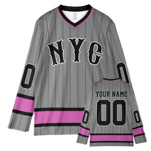 Op de afbeelding: Een shirt met lange mouwen en V-hals in grijs met zwarte krijtstrepen, voorzien van de tekst NYC in het zwart op de voorzijde. De mouwen en zoom hebben roze en zwarte horizontale strepen. Een kleine weergave toont de achterkant met YOUR NAME en 00.