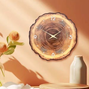 Peut inclure: Une horloge murale ronde avec un design en tranche de bois. Le cadran de l'horloge présente un motif de grain de bois naturel avec des chiffres blancs et des aiguilles dorées. L'horloge est fixée sur un mur clair, avec des éléments décoratifs au premier plan.