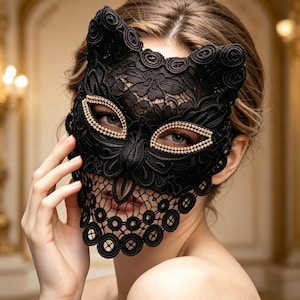 May include: A black lace cat mask featuring intricate floral patterns and pointed ears. The eye openings are outlined with a border of small, clear, sparkling rhinestones, and the lace extends downward to cover the nose and upper cheek area.