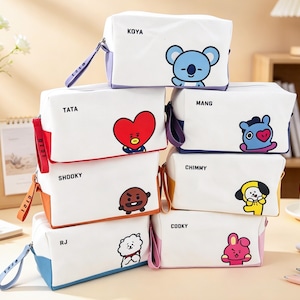 Könnte beinhalten: Ein Stapel weißer, rechteckiger Kosmetiktaschen mit farbenfrohen Akzenten und Cartoon-Charakter-Designs. Jede Tasche hat einen anderen Charakter und Namen aufgedruckt, darunter Koya, Tata, Shooky, RJ, Mang, Chimmy und Cooky.
