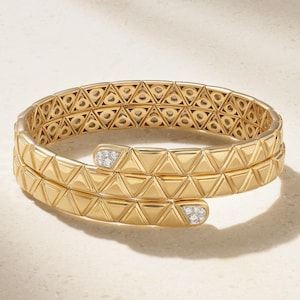 May include: A gold wrap-around bracelet featuring a repeating geometric triangular pattern across the band. The two ends of the bracelet are rounded and inlaid with small, clear, sparkling stones, creating a continuous coil design.