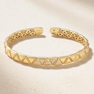 May include: A gold cuff bracelet featuring a repeating geometric pattern of triangular links. Alternating triangles are set with small clear stones. The interior is engraved with Marina B, 750, MB, and the serial number 425040 on the open ends.