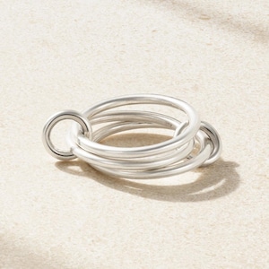 May include: A silver ring featuring a design of intertwined circular bands. The ring has a smooth, metallic finish and a contemporary, minimalist style. The ring is likely made of metal and is suitable for everyday wear.
